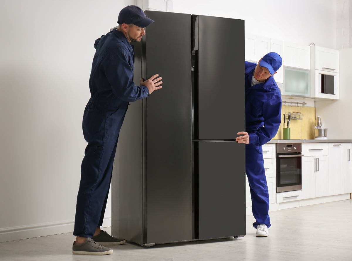 Two men standing next to a black refrigerator in their home.