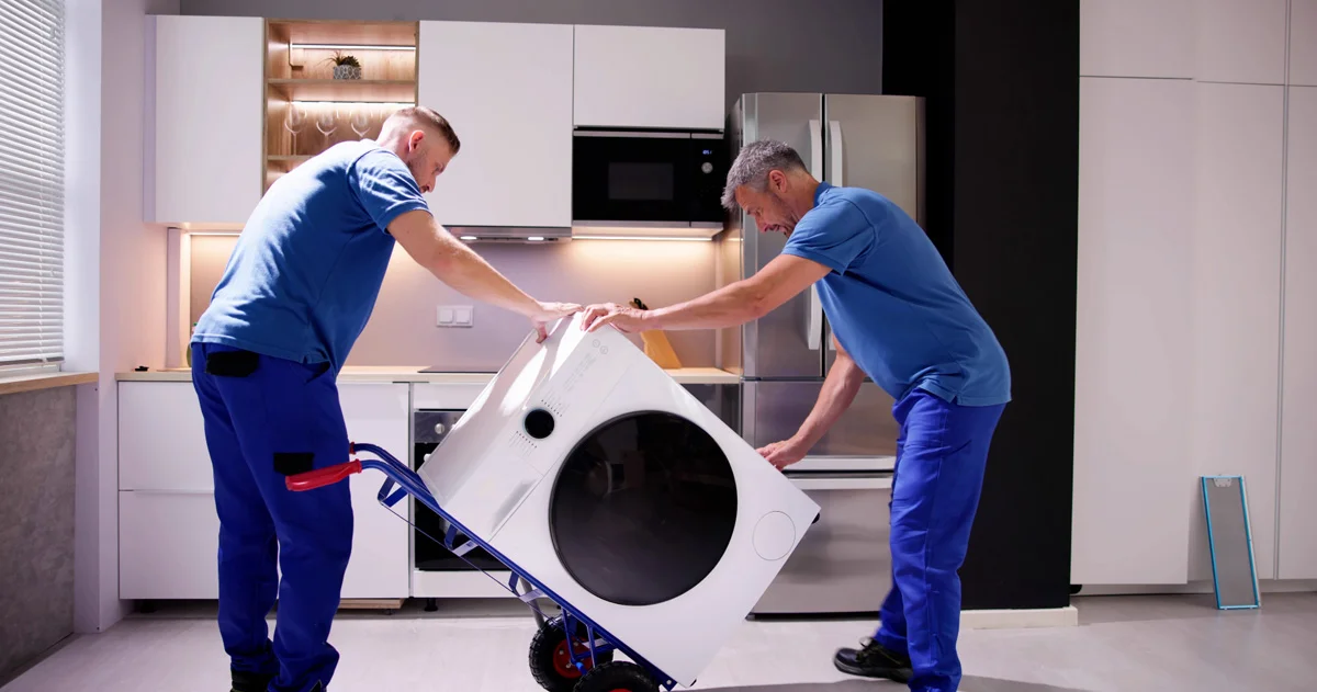 Two men moving a washing machine in a home kitchen.