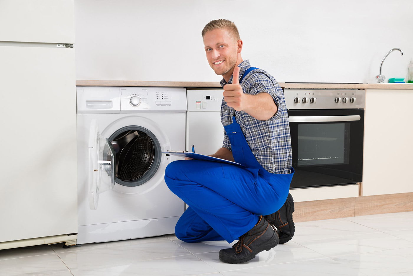 A man in blue overalls about to fix a washing machine.