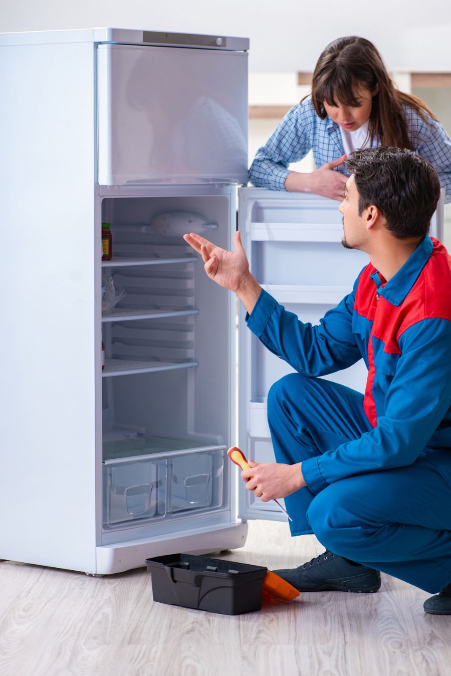 A man and a woman, appliance movers, looking at a refrigerator.