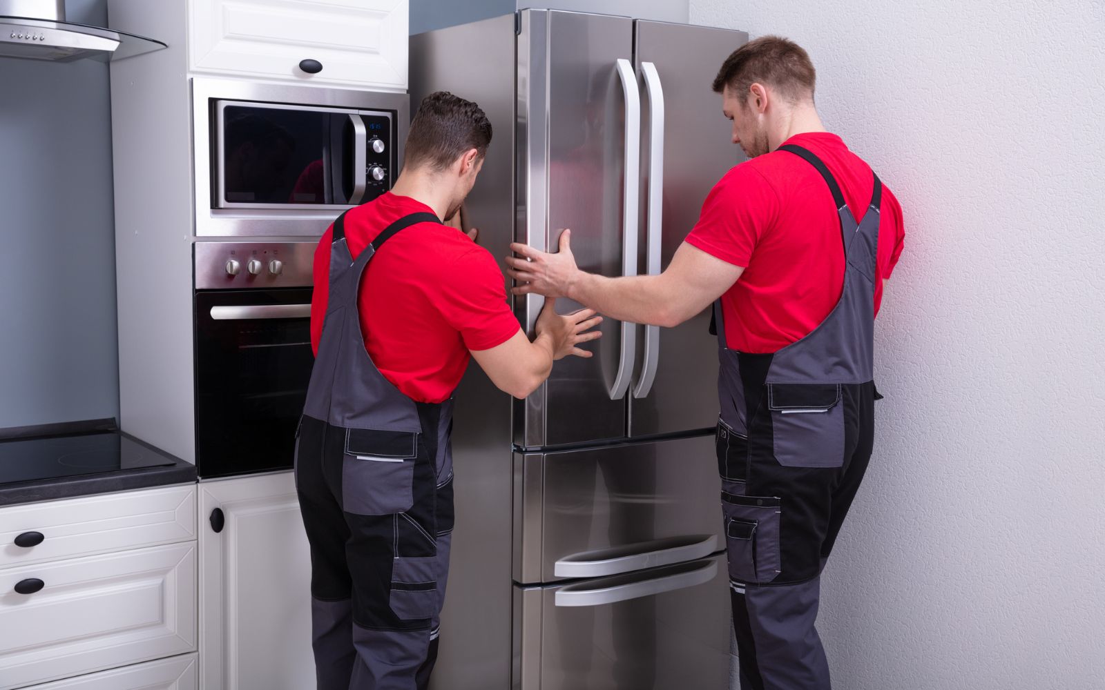 Two appliance movers fixing a refrigerator in a kitchen.