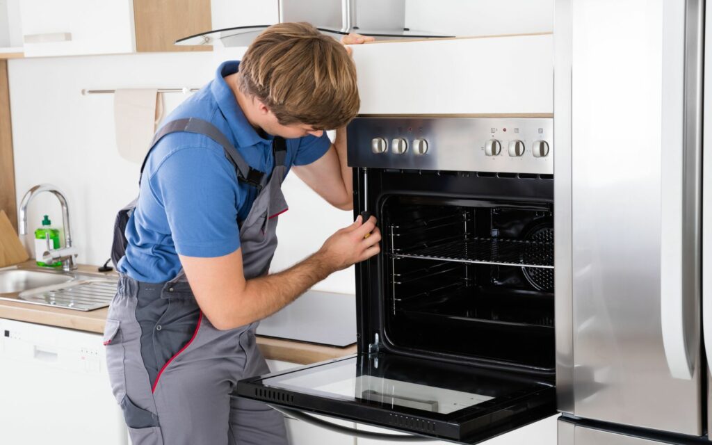 A man repairing a heavy appliance in a kitchen using oven repair skills.