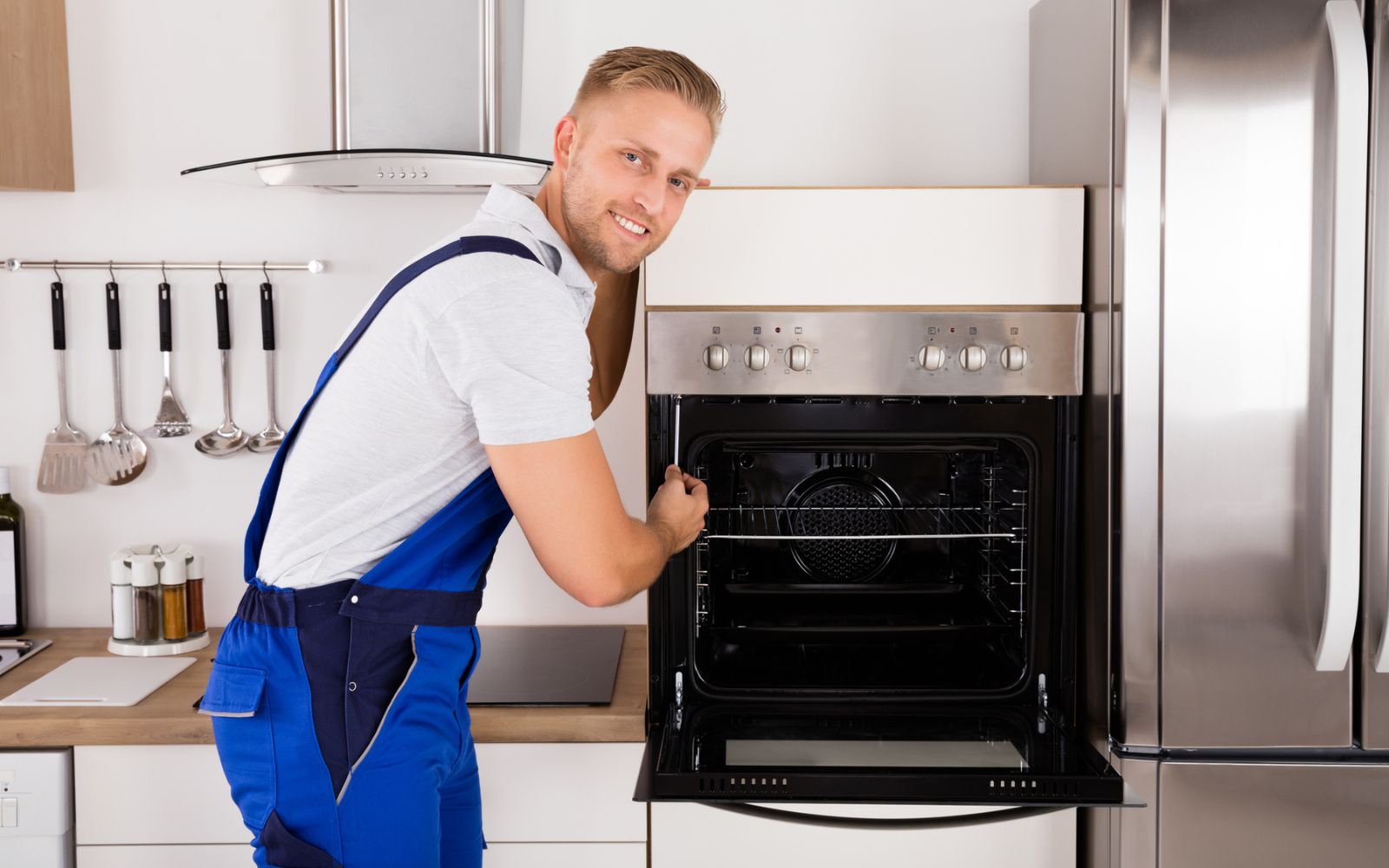 A man, equipped with heavy appliance movers, opening the oven door in a kitchen.