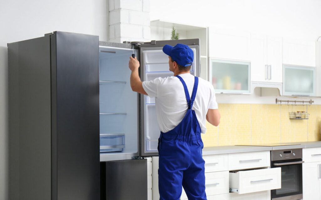 A man, equipped with heavy appliance movers, fixing a refrigerator in a kitchen.