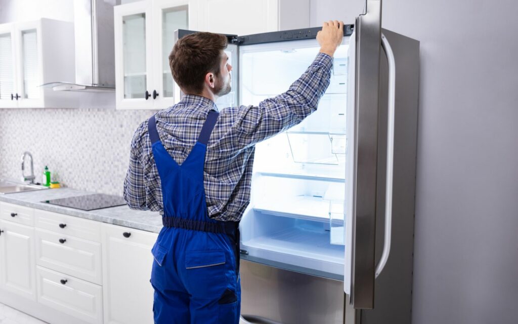 A man using heavy appliance movers opening the door of a refrigerator.